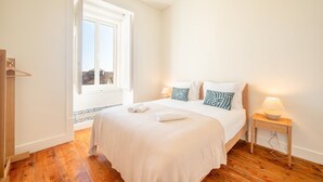 Un dormitorio con una cama grande, dos mesitas de noche, una ventana y suelo de madera.