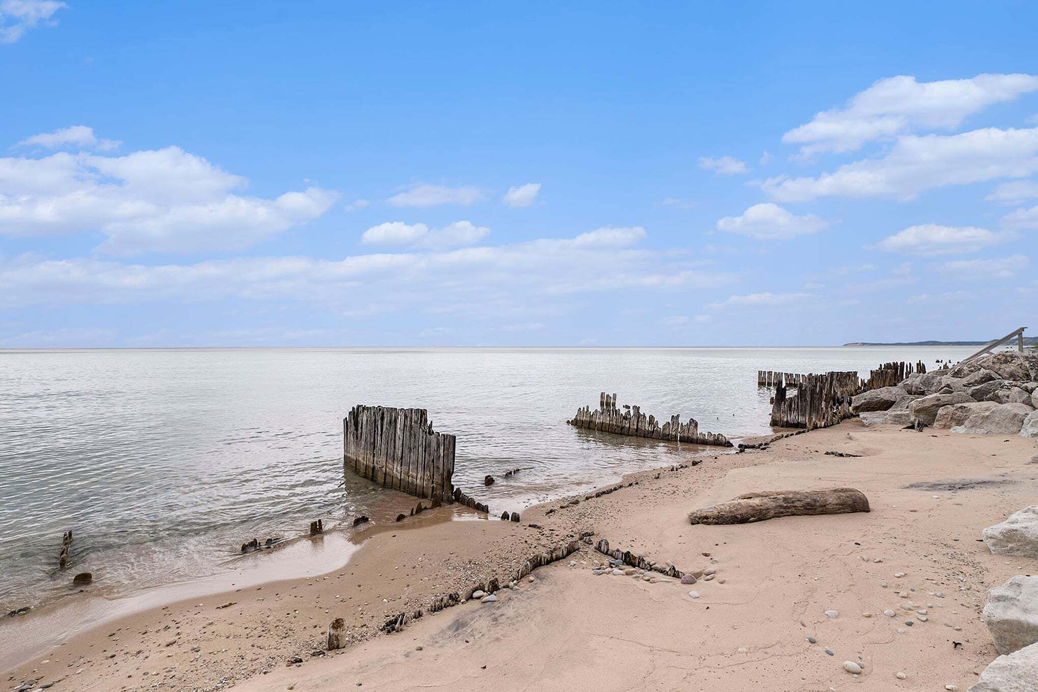 Een strand met houten constructies, kalm water en een heldere lucht.