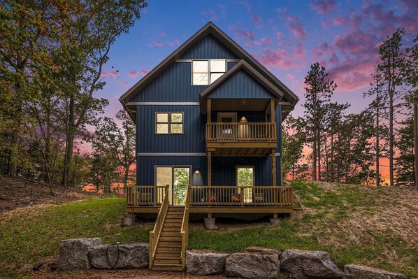 Eine zweistöckige Holzhütte mit Balkon, Treppe und Blick auf den umliegenden Wald.