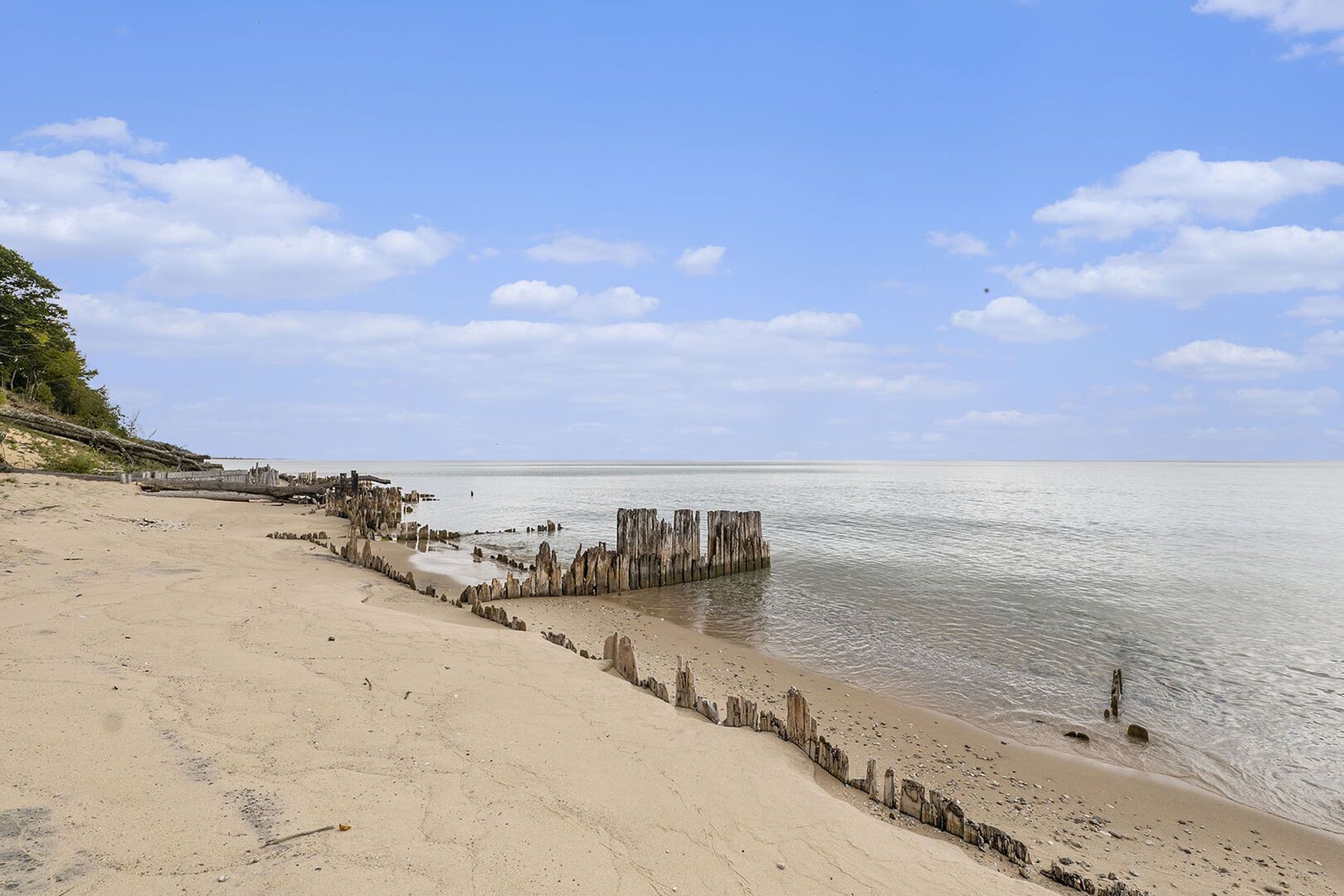 A beach with a wooden structure extending into the water, a sandy shore, and a clear sky.