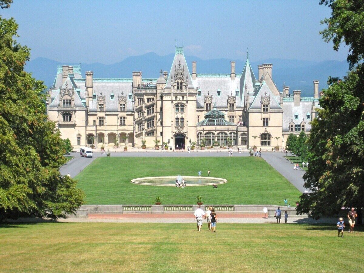 A large, historic building with a central courtyard, surrounded by lush greenery and a clear sky.