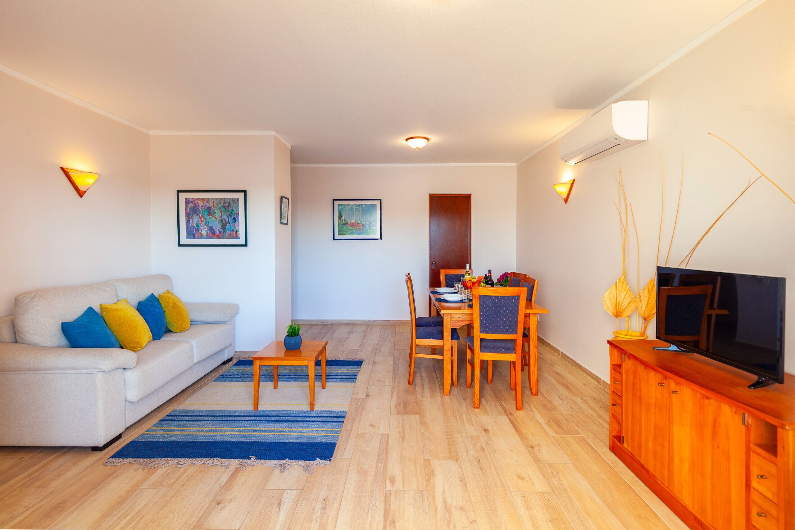 A living room with a sofa, dining table, chairs, and a TV on a wooden cabinet.