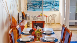 A dining area with a view of a marina, a table set with plates, glasses, and a fruit bowl. - Apartment Portobello (Loulé)