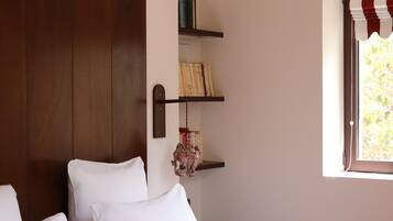 Un dormitorio con una cama grande, cabecera de madera, pared de acento rojo, ventana con cortinas a rayas y una lámpara colgante.
