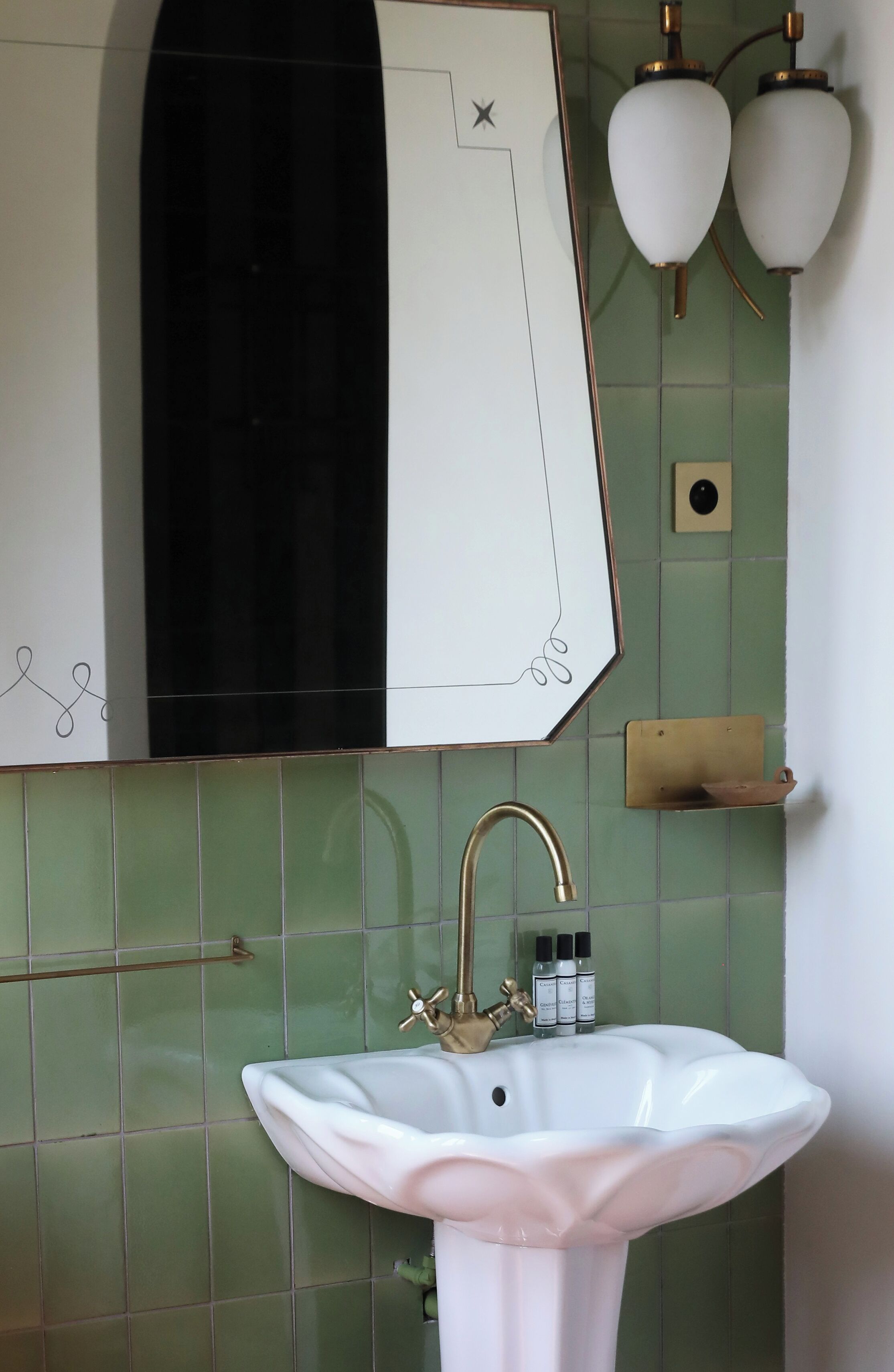 Un bagno con un lavandino bianco, uno specchio e pareti rivestite di piastrelle verdi.