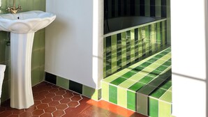 Ein Badezimmer mit einem weißen Waschbecken, grünen Fliesen und einer Duschkabine.