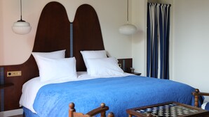 Ein ordentlich bezogenes Bett mit blauer Decke, einem hölzernen Kopfteil und zwei Nachttischlampen.