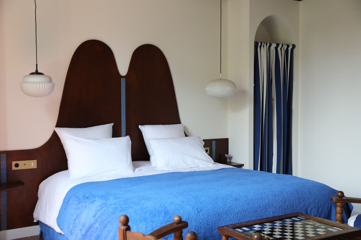 A neatly made bed with a blue blanket, a wooden headboard, and two bedside lamps.