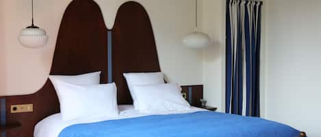 A neatly made bed with a blue blanket, a wooden headboard, and two bedside lamps.