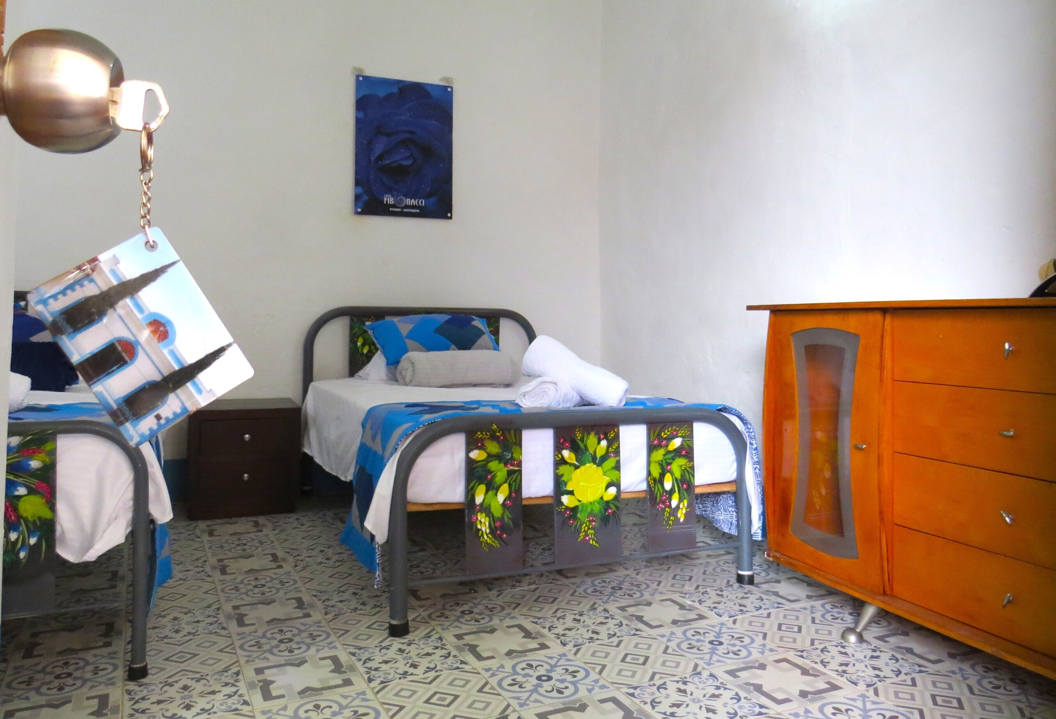 A room with two beds, a wooden cabinet, and patterned floor tiles.