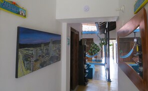 A hallway with a cityscape painting, a wooden door, a blue hammock, and a blue sofa. - Casa Fibonacci (Titiribí)