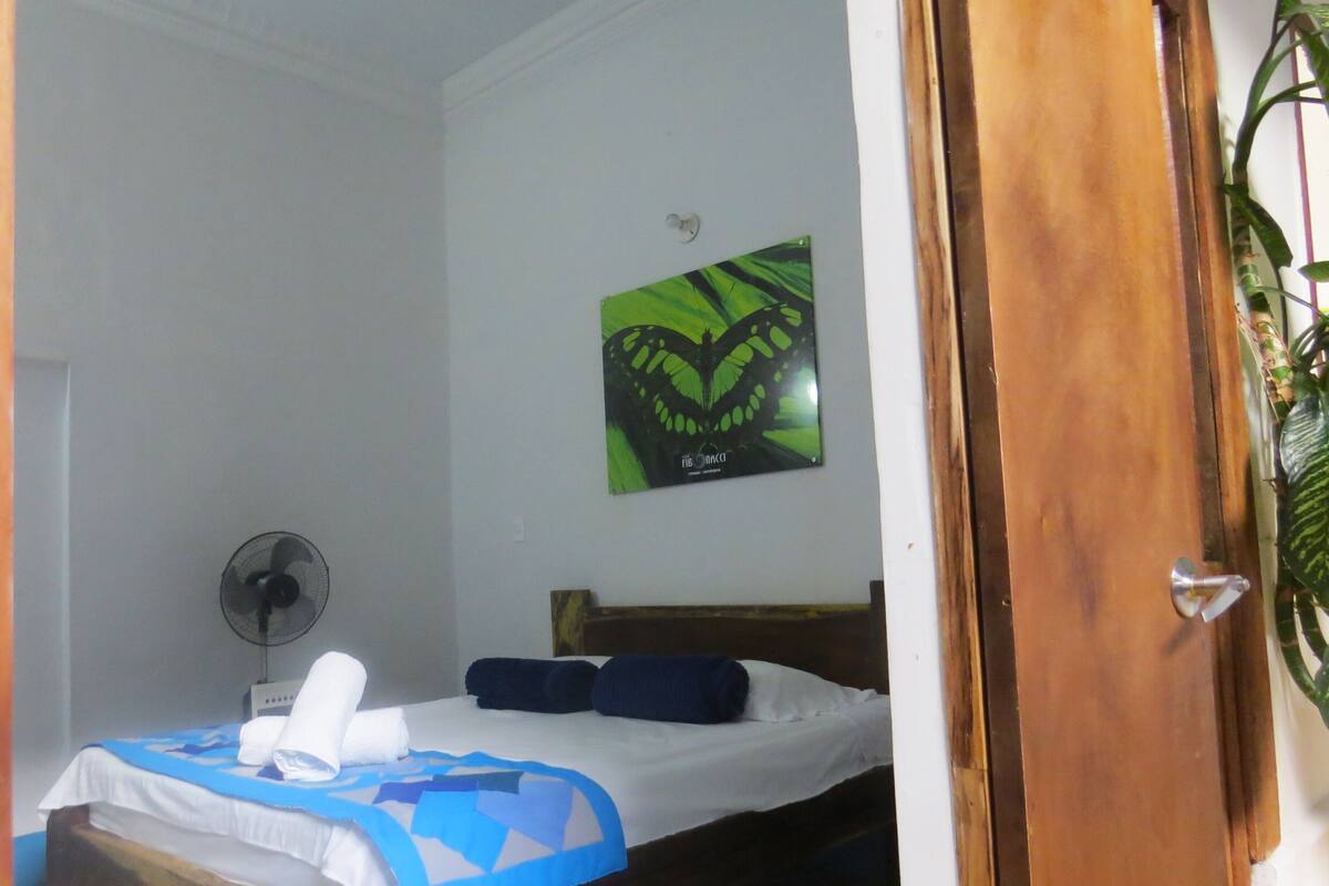 A bedroom with a bed, a wall-mounted fan, and a green butterfly artwork.