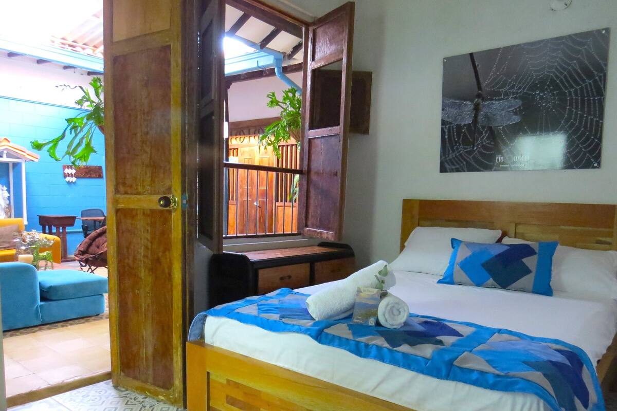 A bedroom with a bed, pillows, a wall-mounted artwork, and a door leading to another room.