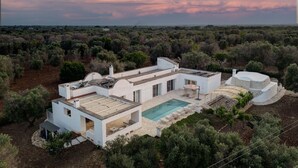 A modern villa with a swimming pool, terraced roof, and a stone structure.