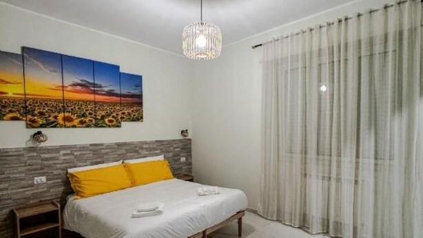 Une chambre à coucher avec un lit, un tableau accroché au mur, un luminaire suspendu et une fenêtre avec des rideaux.