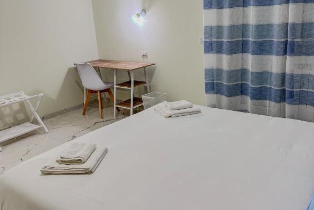 A hotel room with a bed, a desk, a chair, and a window with striped curtains.