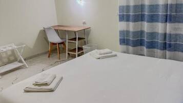 A hotel room with a bed, a desk, a chair, and a window with striped curtains.