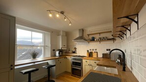Une cuisine moderne dotée d’une grande fenêtre, de plans de travail en bois, d’une cuisinière à gaz et de tabourets de bar.