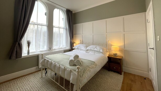 Une chambre à coucher avec un lit, des lampes de chevet, une fenêtre avec des rideaux et un radiateur.