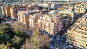 A densely packed urban area with multi-story residential buildings, a visible street with parked cars, and a clear view of distant mountains. - Penthouse in the center of Rome, with terrace a few meters from the Conca d'oro Metro.  (Roma)