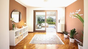 A modern interior with a wooden floor, a white console table with a mirror, a patterned rug, and potted plants.