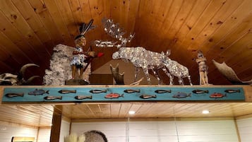 A wooden ceiling with a decorative elk and fish motif, a shelf with fish carvings, and a rustic interior with wooden walls and a hanging pot rack.