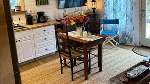 Un interior acogedor con techo de madera, una mesa de comedor con sillas, un televisor montado en la pared y un ventanal con cortinas.