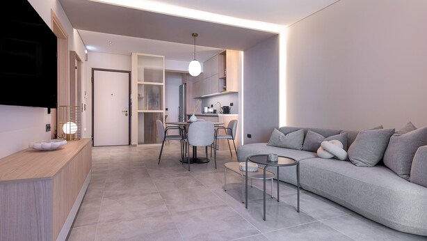 A modern living room with a grey sofa, a coffee table, and a dining area with chairs and a table. - Phaedrus Living: Athens Luxury Residences Champagne (Athens)