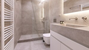 A modern bathroom with a glass-enclosed shower, a white toilet, and a vanity with a mirror and towel rack. - Phaedrus Living: Athens Luxury Residences Champagne (Athens)