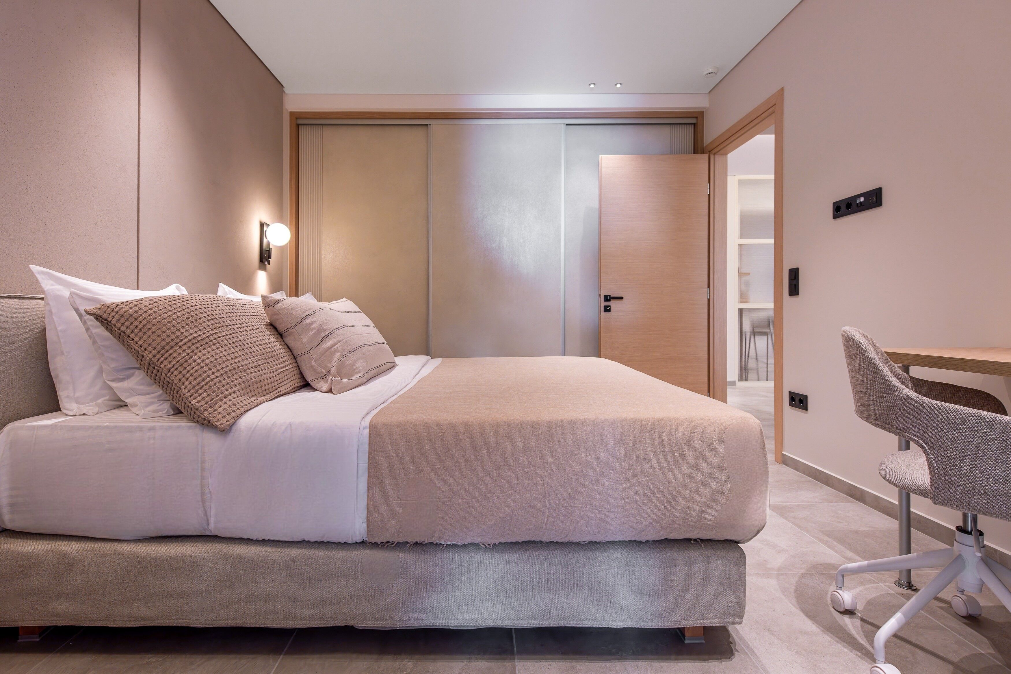 A modern bedroom with a bed, bedside table, and a desk with a chair.