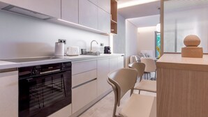 A modern kitchen with built-in appliances, a dining area with chairs, and a window with blinds. - Phaedrus Living: Athens Luxury Residences Champagne (Athens)