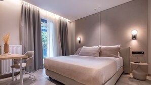 A modern bedroom with a large bed, a desk, and a chair. There are two wall-mounted lights and a window with curtains. - Phaedrus Living: Athens Luxury Residences Champagne (Athens)