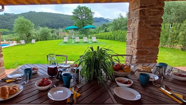 A patio table set for breakfast with a view of a lush garden and a pool. - Villa / Independent home in Capannori with 3 bedrooms sleeps 6 (Capannori)