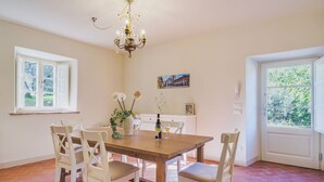 A dining area with a wooden table, white chairs, a chandelier, and a window with a view of greenery. - Villa / Independent home in Capannori with 3 bedrooms sleeps 6 (Capannori)