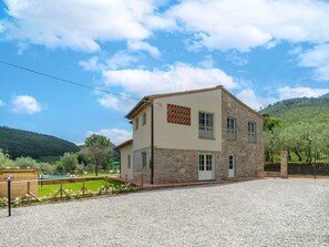 Une maison en pierre à deux étages, avec une allée en gravier et une piscine à l’arrière.