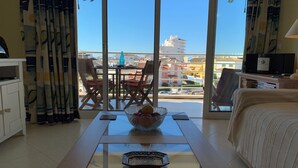 Habitación de hotel con balcón, una mesa de comedor con sillas, un televisor y una cama.