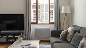 A living room with a flat-screen TV, a grey sofa, a floor lamp, a radiator, and a window with curtains. - L'Authentique - A Journey to Provence (Aix-en-Provence)