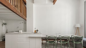 A modern kitchen with white cabinetry, a dining area with green chairs, and a staircase with wooden railings. - L'Authentique - A Journey to Provence (Aix-en-Provence)