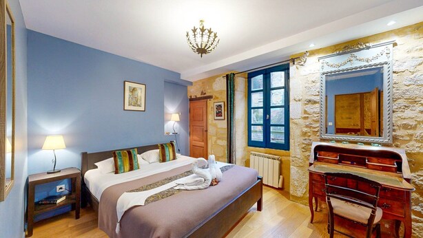 A bedroom with a bed, bedside table, lamp, dresser, and a large mirror. - Les Fables de la Fontaine (Sarlat-la-Canéda)