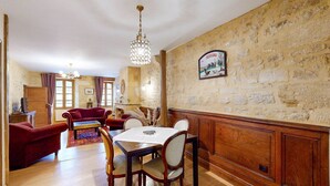 A dining area with a wooden table and chairs, a chandelier, and a stone wall with a sign. - Les Fables de la Fontaine (Sarlat-la-Canéda)