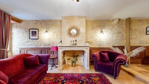 A room with a fireplace, two red sofas, a patterned rug, and stone walls. - Les Fables de la Fontaine (Sarlat-la-Canéda)