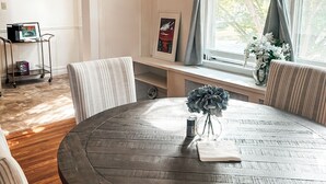 A round wooden table with a vase and a spool of thread, surrounded by striped chairs, in a room with a window and a shelf with a picture frame. - 3BR Home in Downtown Saratoga - Walkable location - Close to Racetrack (Saratoga Springs)