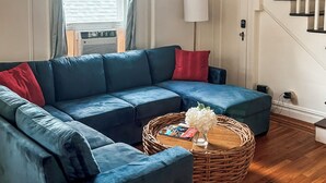 A living room with a blue sectional sofa, a wicker coffee table, and a staircase. - 3BR Home in Downtown Saratoga - Walkable location - Close to Racetrack (Saratoga Springs)