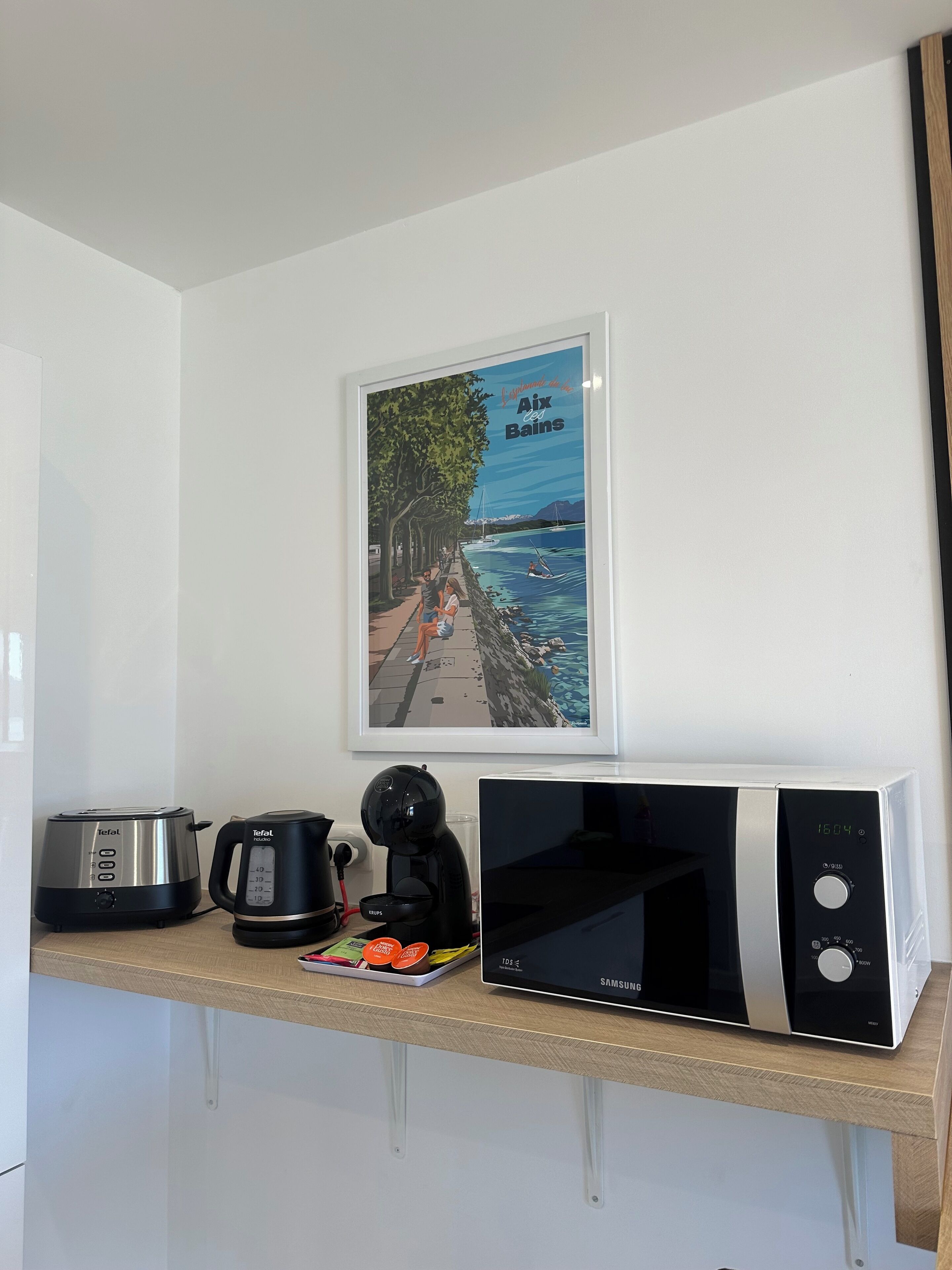 Een keuken met een Toefal-toaster, een Toefal-koffiezetapparaat, een Samsung-magnetron en een lijst met een afbeelding van een zeegezicht.