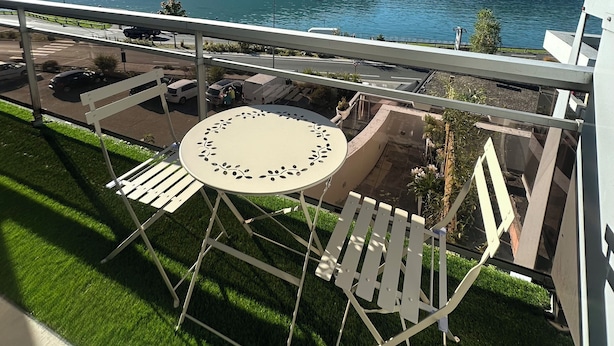 En balkon med bord og stole med udsigt over en sø og bjerge.