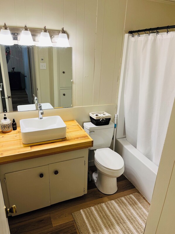 A bathroom with a wooden vanity, white sink, and a toilet. There is a mirror above the sink and a shower curtain.