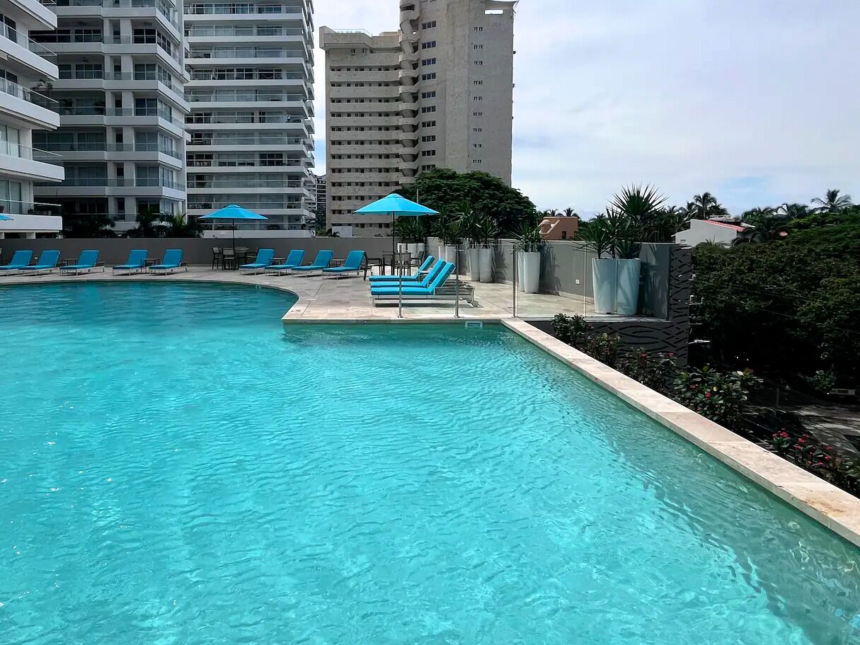 A swimming pool with lounge chairs and umbrellas, surrounded by high-rise buildings.
