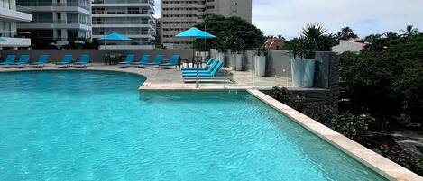 A swimming pool with lounge chairs and umbrellas, surrounded by high-rise buildings.