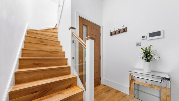 Una escalera de madera con barandillas de vidrio, una puerta de madera y una pequeña consola blanca con una planta.