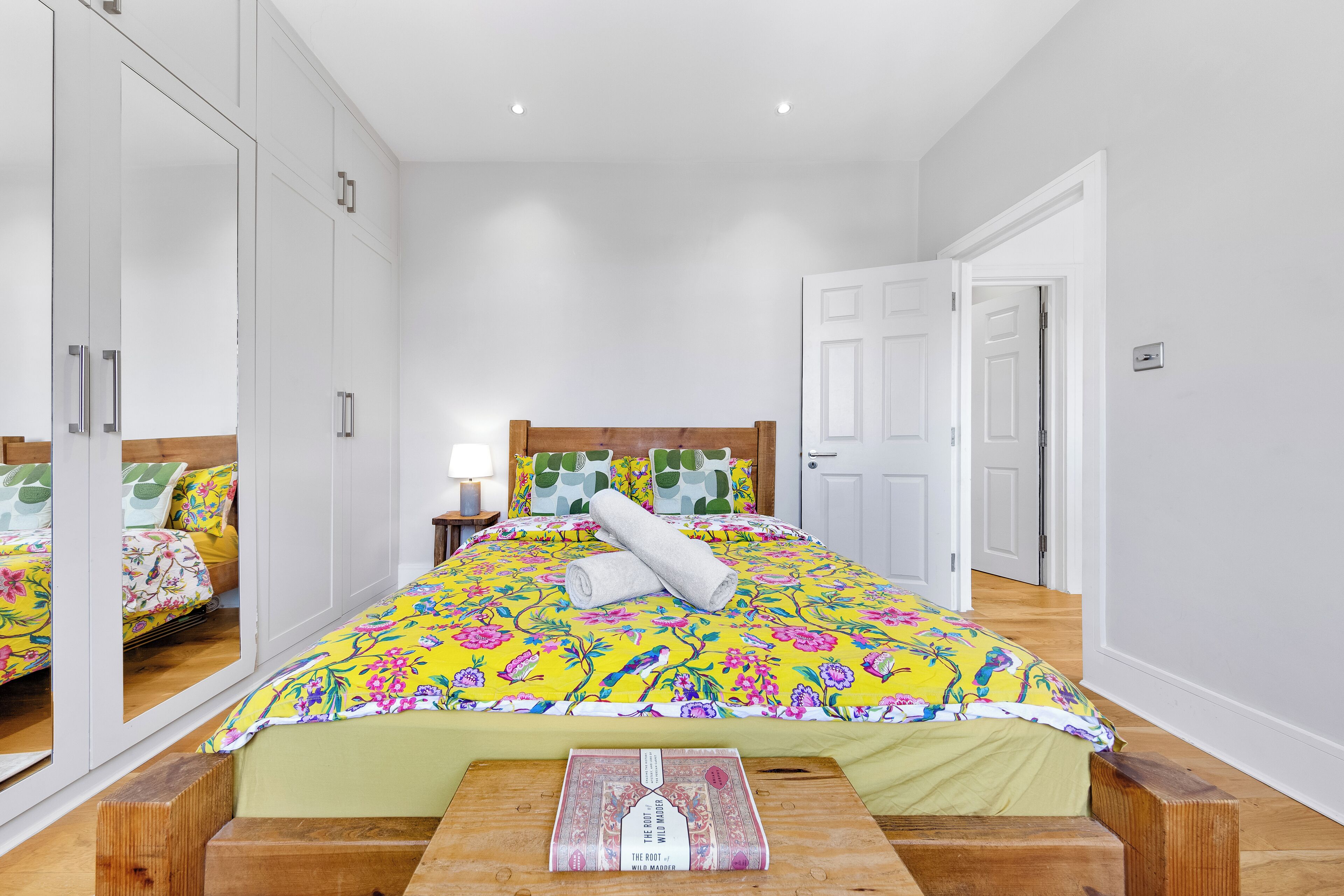 A bedroom with a bed, a nightstand, a mirror, and a wooden bench.
